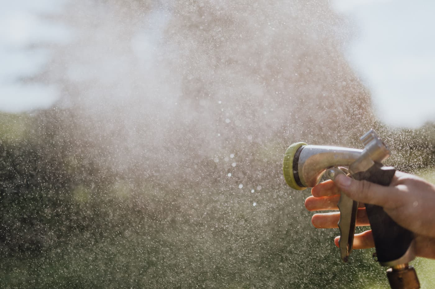 A hand holding a spray nozzle, water misting from the tip